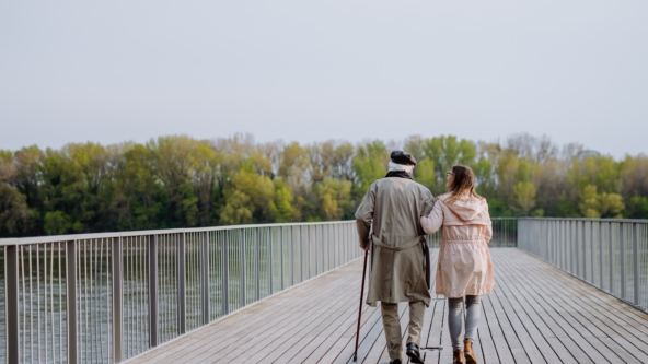 Rear view of senior man with daughter outdoors on a walk on pier by river.